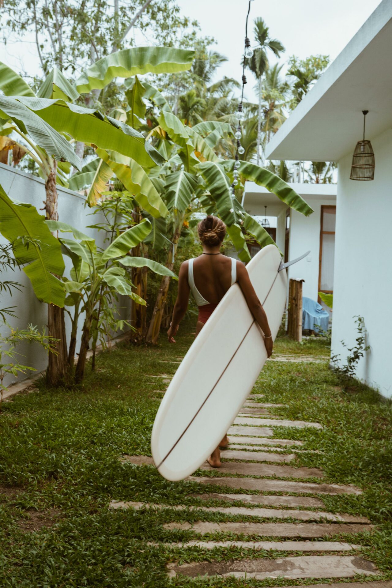 Surfista caminando con su tabla entre vegetación tropical